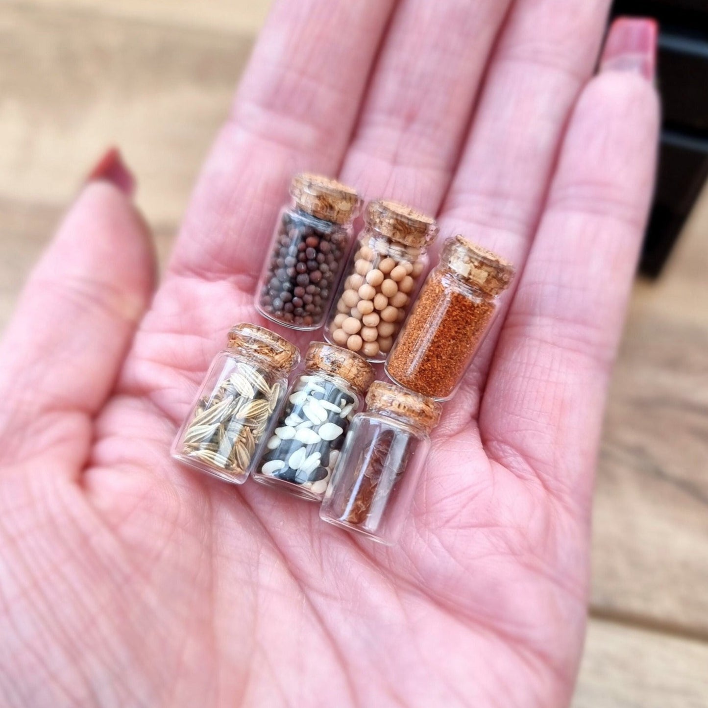 Set of 1:12 scale miniature apothecary jars with cork lids held in an open palm. Jars contain different herbs and spices