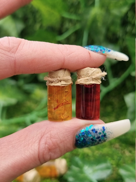 A miniature jar of shredded orange marmalade and a miniature jar of crimson jam with brown paper lids are show held side by sidebetween a forefinger and thumb against a green background