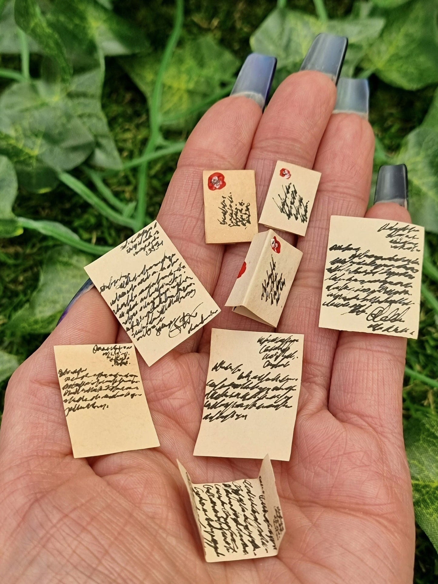 8 1:12 scale miniature aged letters are displayed in the open palm of a hand. 2 letters are part written, 2 are fully written, 2 are sealed letters and 2 are opened letters. A finger points to a sealed letter to show scale. 