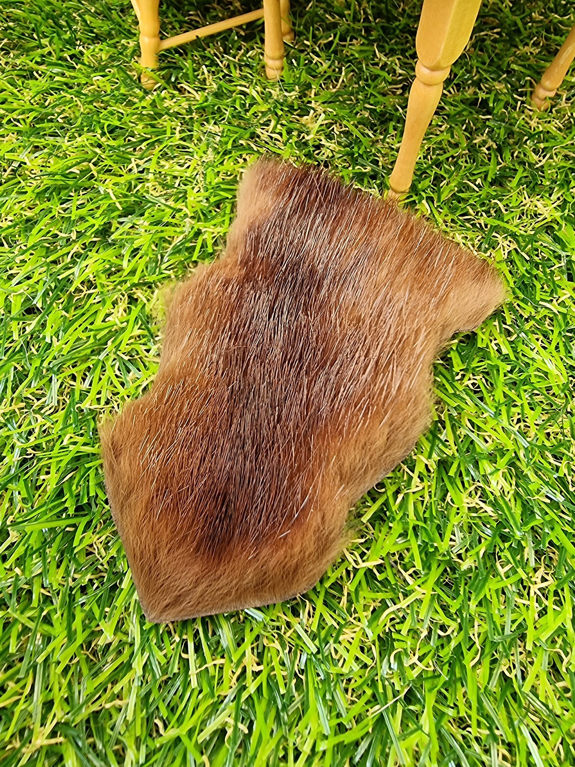 1:12 scale dark brown animal skin genuine fur rug on a green grass floor with miniature table in the background. The rug is dark brown with lighter areas to the edges