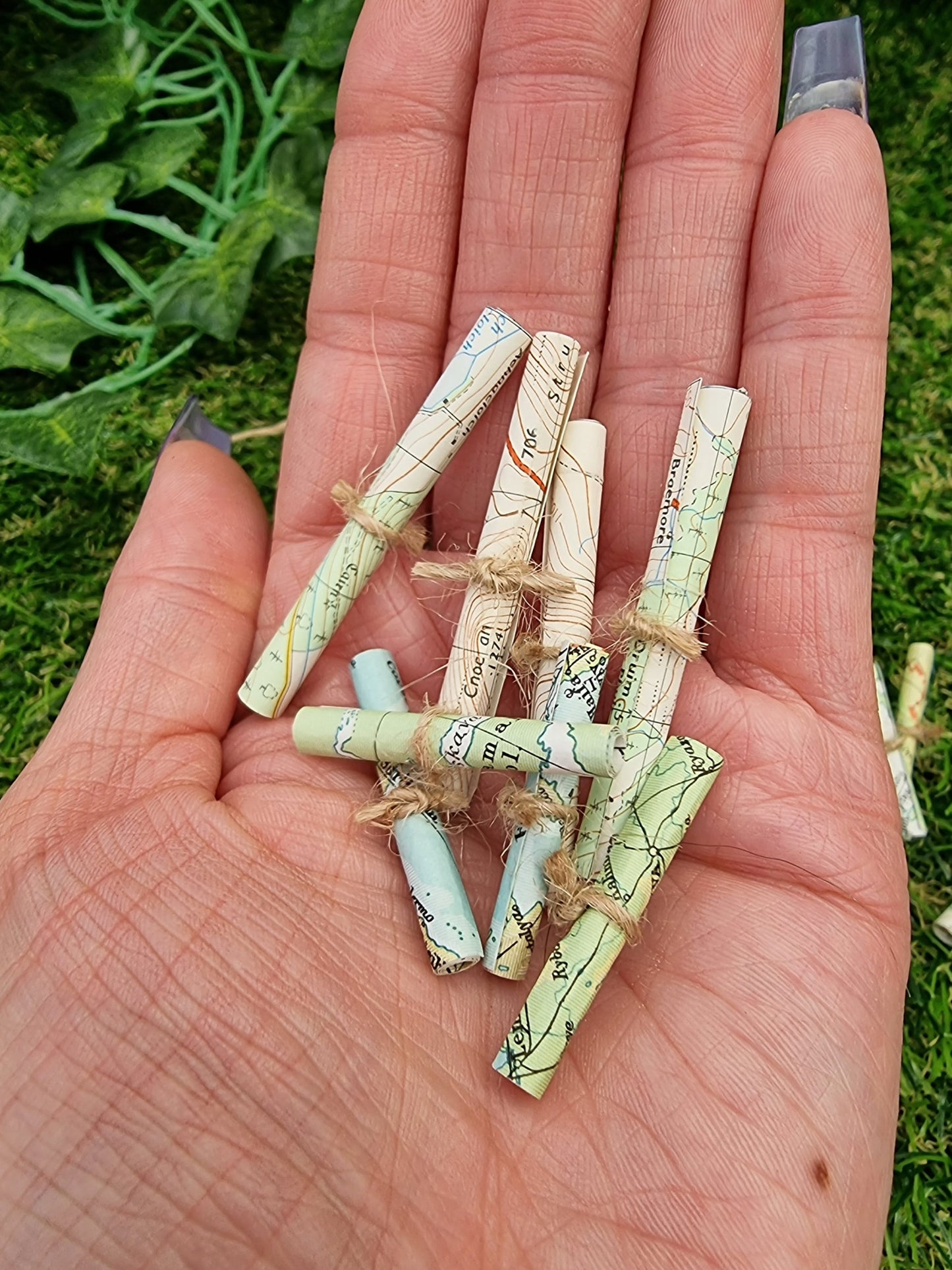 1:12 scale Miniature map scrolls tied with jute string are displayed in the palm of a hand. The maps are mainly coloured white, green and blue