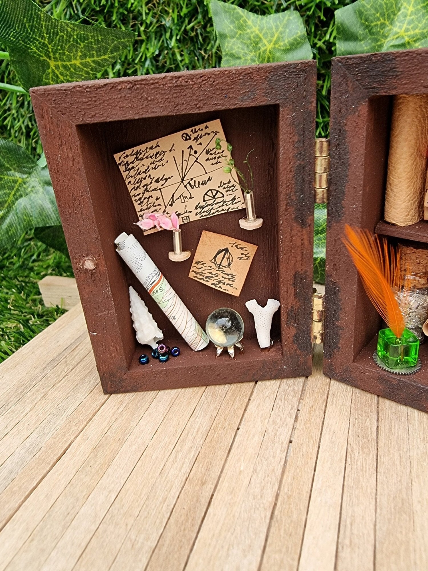 Detail shown of a 1:12 scale miniature brown apothecary cabinet. The left cabinet door has aged notes, shells, crystal ball, map, coral and vases. A finger points for scale