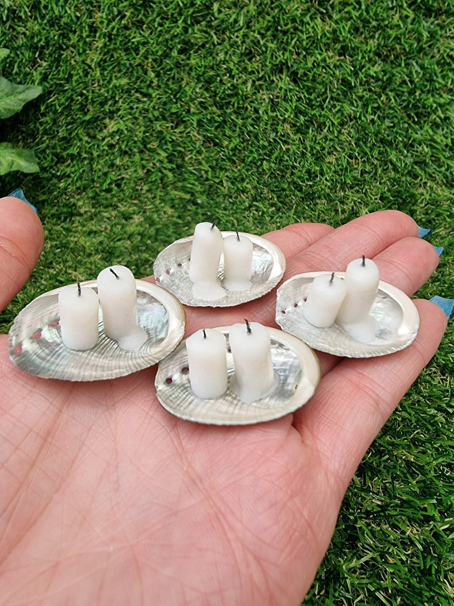 Four miniature 1:12 scale abalone shell dishes, each with Two white miniature candles. Displayed in an open hand