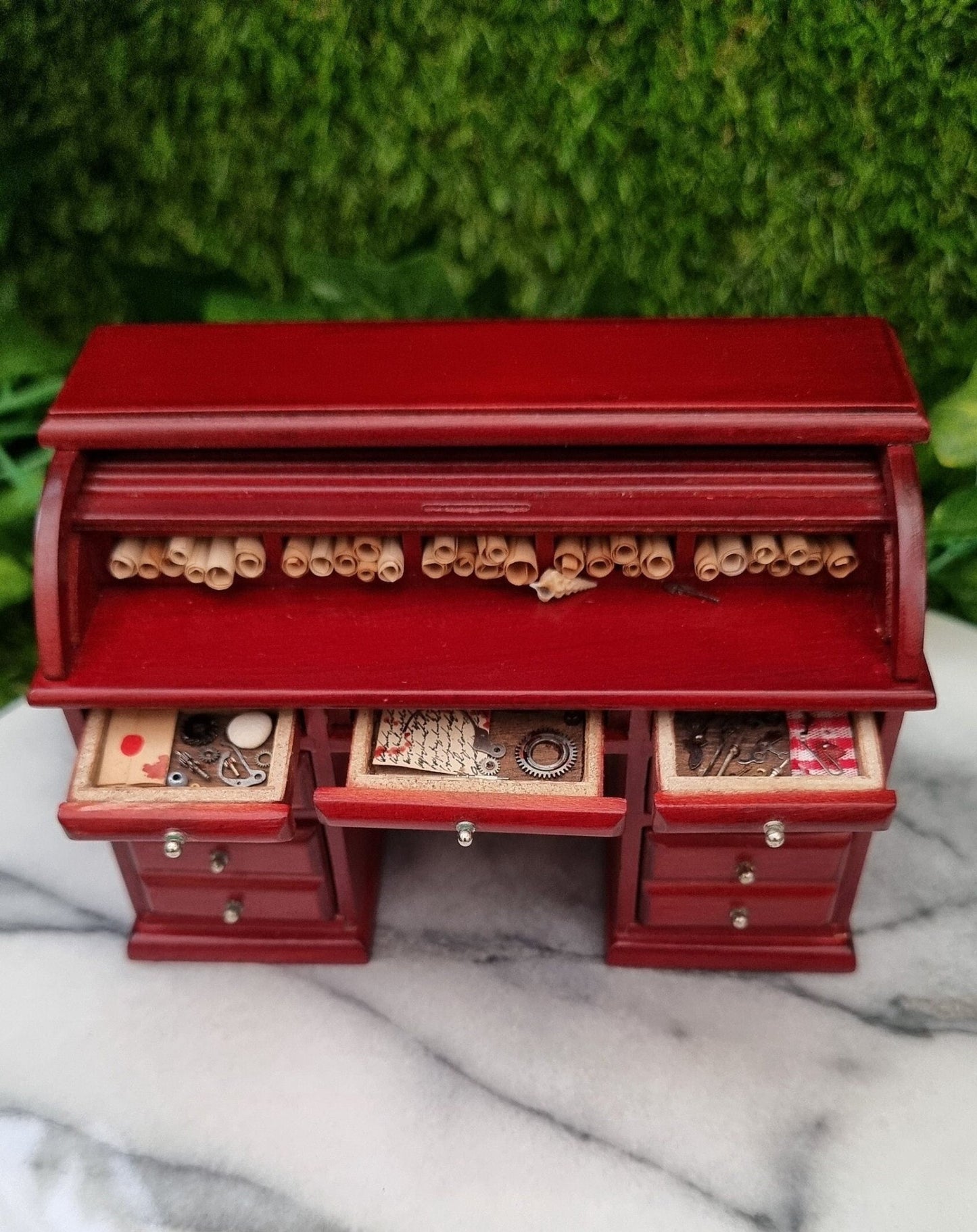 1:12 scale brown rolltop desk  with three open drawers and open rolltop. The desk top is filled with parchment rolls and the drawersare filled with bloody parchments and metal tools