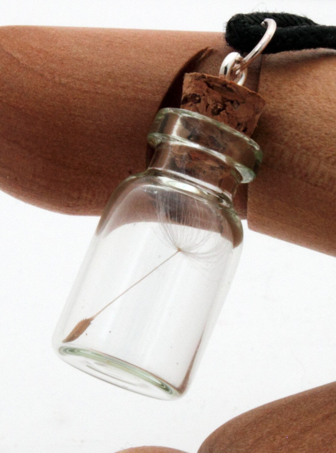 A glass vial necklace contains a single dandelion seed. The dandelion vial hangs on a fine sterling silver chain and is displayed on an articulated wooden hand against a white background