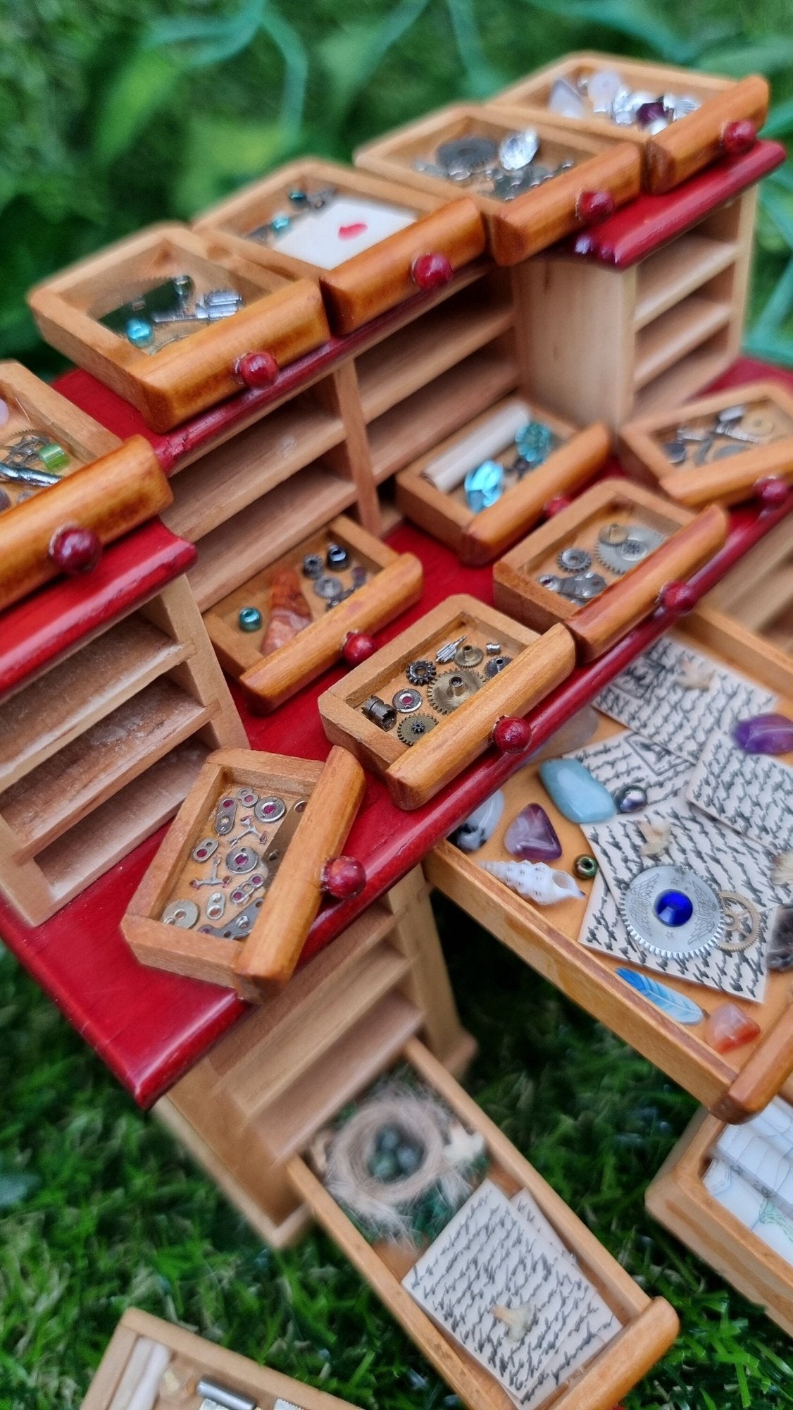 Detail of a 1:12 scale desk with 21 drawers has all drawers removed and on display. Each drawer is filled with different items, including parchments, shells,  letters, quill, gemstones, nest, trinkets and curios