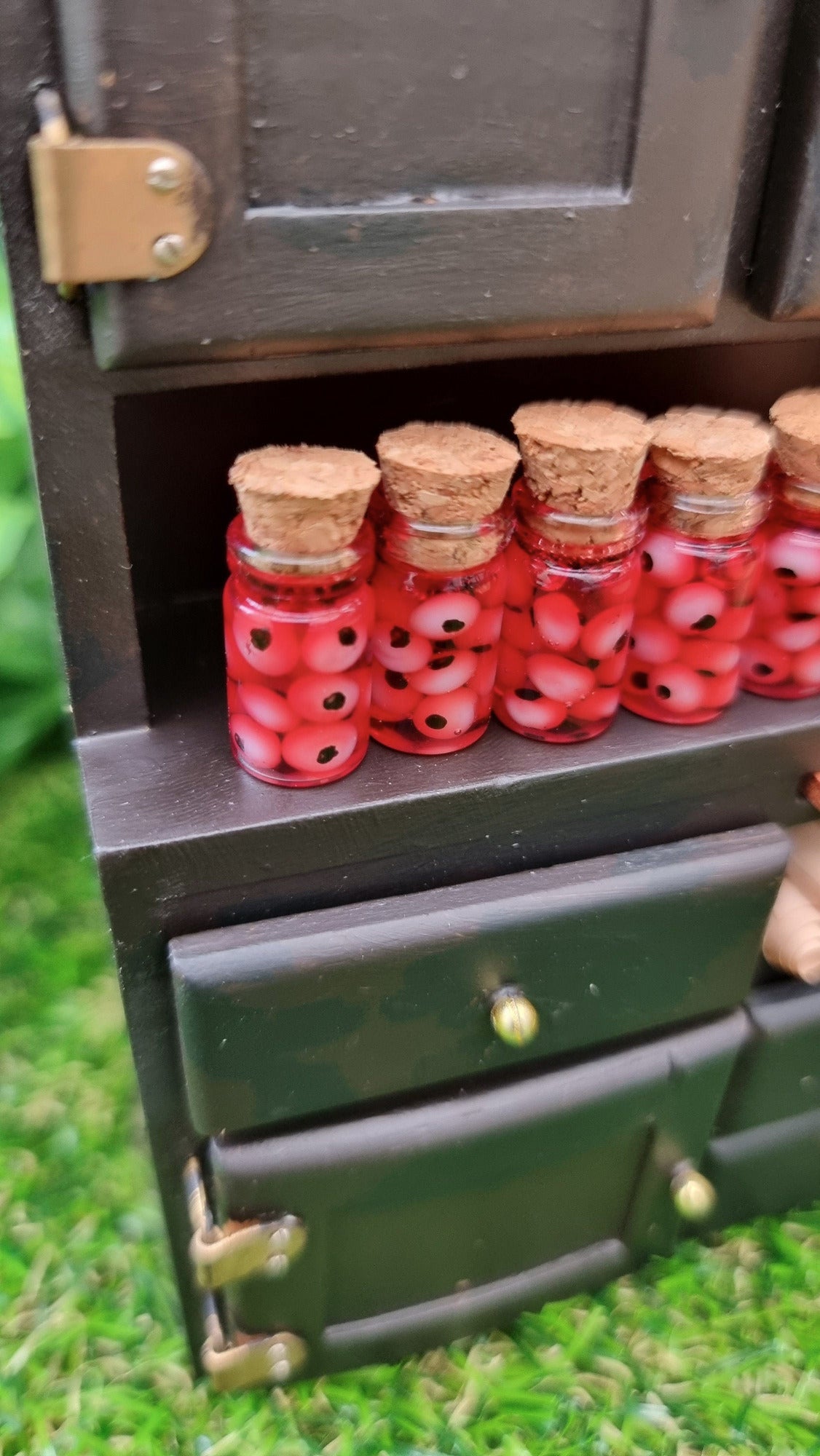 A 1:12 miniature black dresser holds miniature glass jars containing eyeballs and red liquid.  The miniature jars are topped with cork stoppers